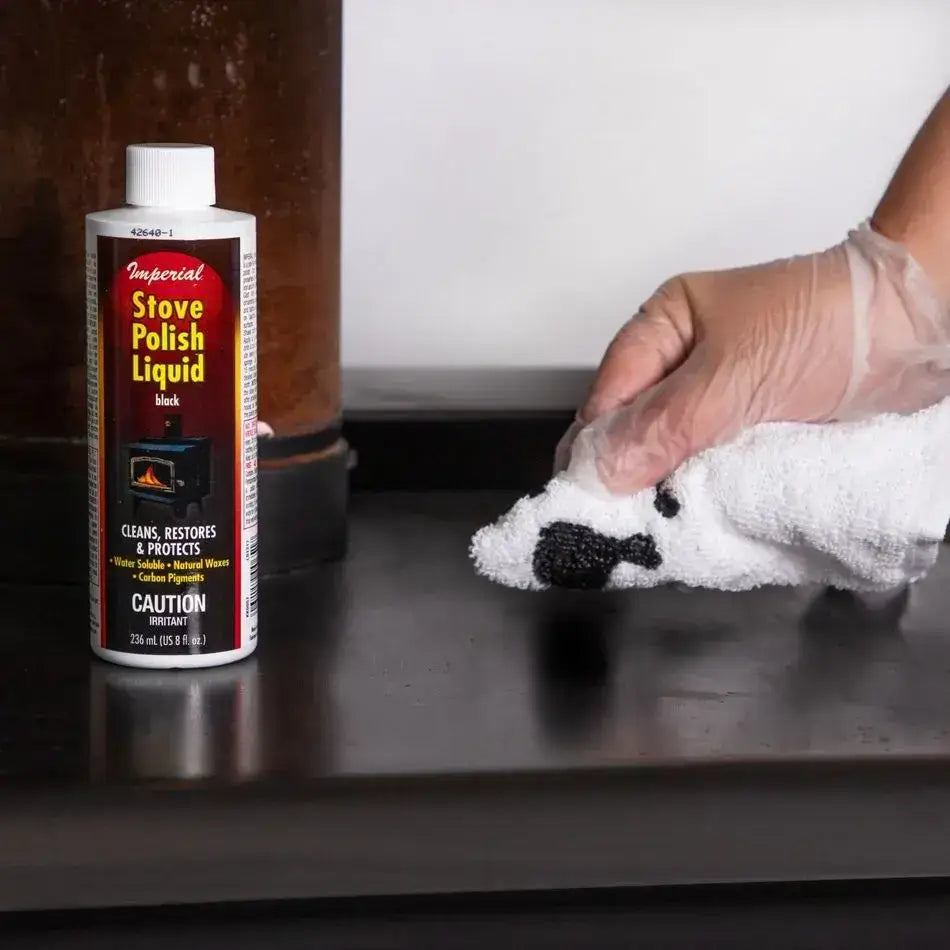 Person applying Imperial 8 fl. oz. Stove Polish Liquid - Black on stove surface. Cabin Depot cleaning product for restoring cast iron or steel.