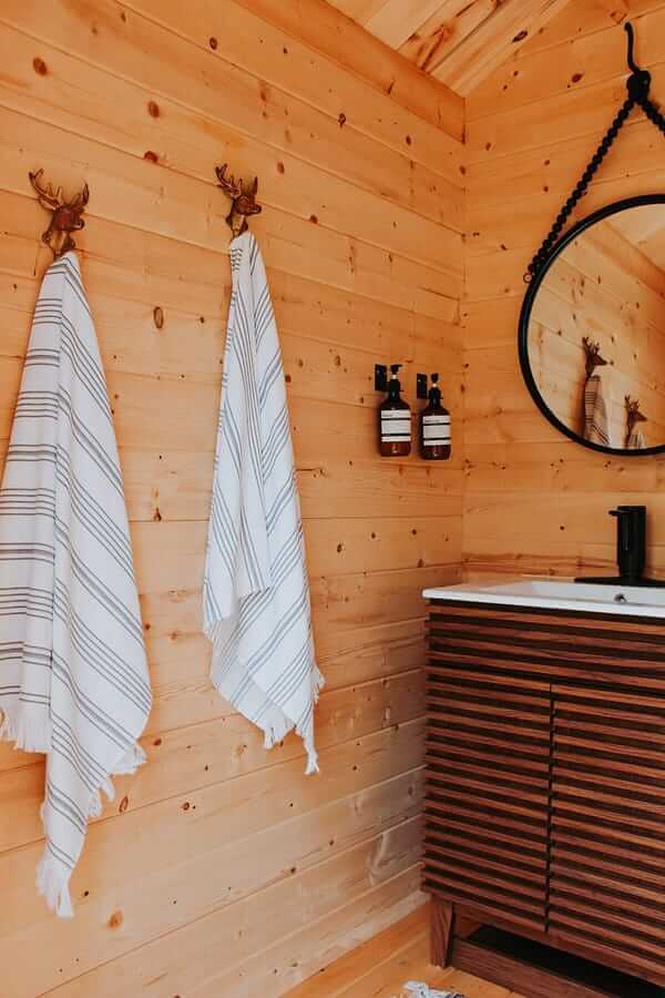 Interior of Loo Loo House with wooden walls, towels on hooks, and a mirror. Multi-use outhouse cabin, Bus Shelter or Tiny Shed by Cabin Depot.