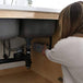 Woman installing Acuva ArrowMax 1.2 UV-LED water purifier under kitchen sink for off-grid water purification.