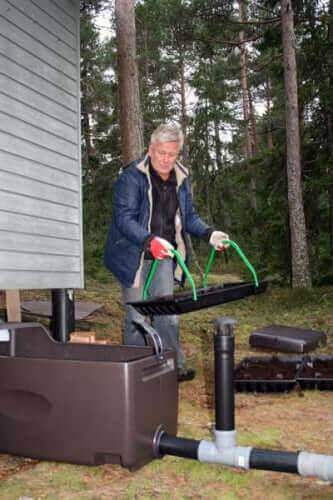 Person installing Biolan Light Greywater Filter System at a cabin with eco-friendly design from Cabin Depot