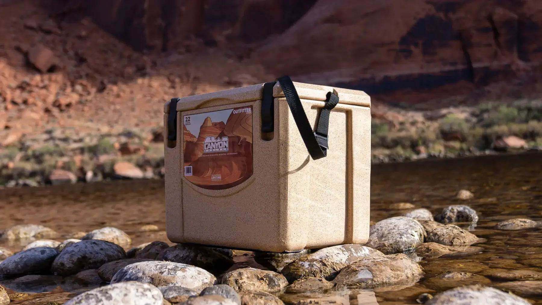 Canyon Coolers 22QT Outfitter Cooler on rocky riverbed, ideal for outdoor adventures; available at Cabin Depot.