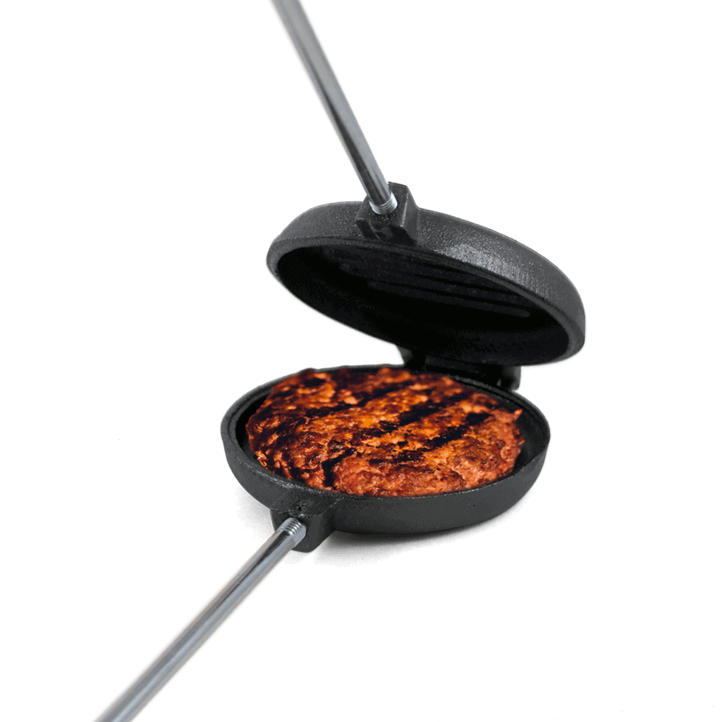 Coghlans Cast Iron Broiler cooking burger, available at Cabin Depot for campfire and barbecue grilling.