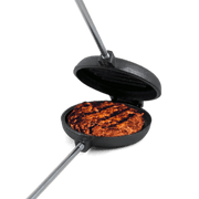 Coghlans Cast Iron Broiler cooking burger, available at Cabin Depot for campfire and barbecue grilling.
