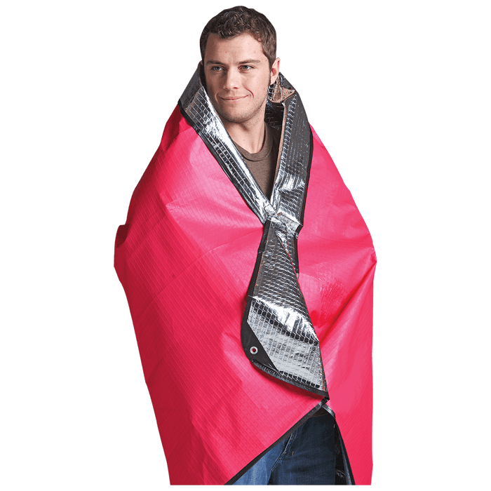 Man wrapped in red Coghlans Thermal Blanket, showing water and windproof features, reinforced with grommets for outdoor use.