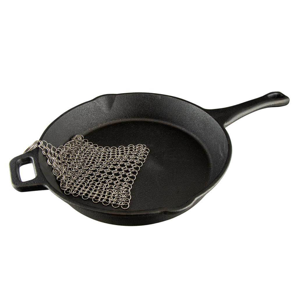 Cast iron skillet with Coghlan's stainless-steel chainmail scrubber, perfect for cleaning cookware while camping. Available at Cabin Depot.