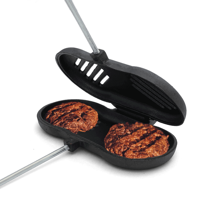 Cast iron broiler with cooked burgers, featuring open slots for grease escape. Ideal for campfire grilling and versatile cooking.