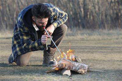 Man using bellow from Coghlan's Fire-in-a-Box kit to start campfire, essential hiking gear, available at Cabin Depot.