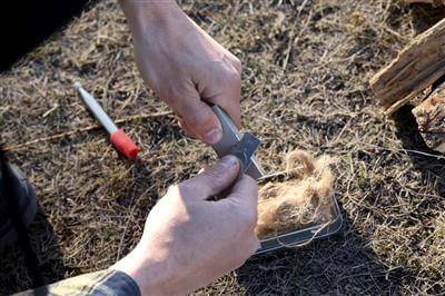 Person using Coghlans Fire-In-A-Box kit with flint rod and tinder, perfect for outdoor enthusiasts from Cabin Depot.