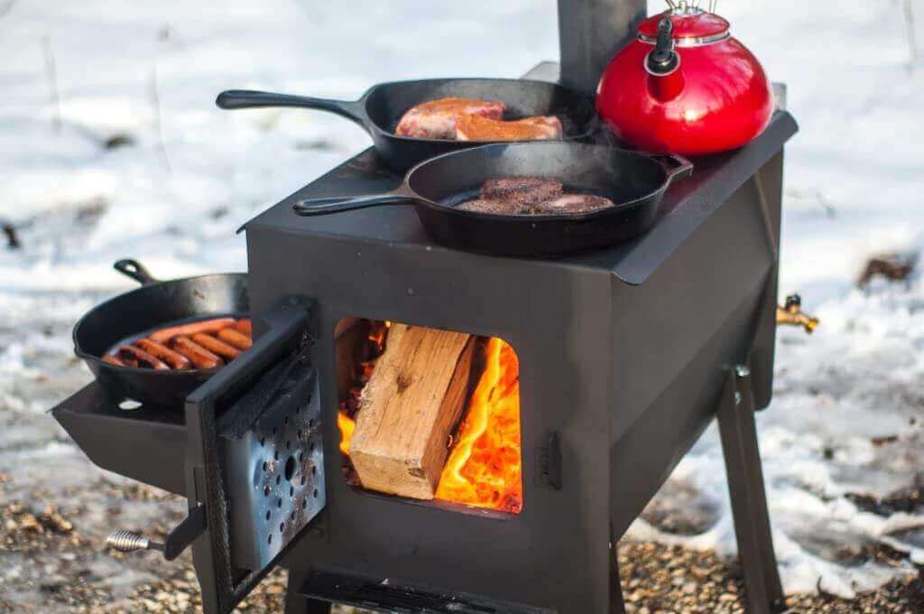 Englander GRIZZLY Camp Stove by Cabin Depot with logs burning, cooking pans, and red kettle, showing durability and efficiency in use.