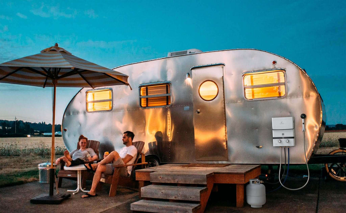 Couple relaxing outside a retro camper with an Eccotemp EL5 Portable Tankless Water Heater at sunset.