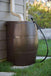 Brown FCMP Outdoor 50Gal Rain Catcher Rain Barrel connected to a downspout beside a house.