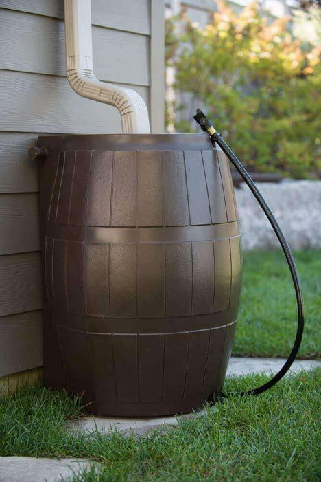 Brown FCMP Outdoor 50Gal Rain Catcher Rain Barrel connected to a downspout beside a house.