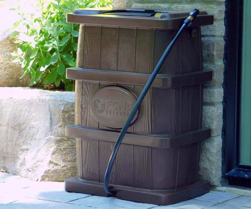 FCMP Outdoor 45Gal Wood Grain Rain Barrel in brown with hose, showcasing slim-line design against a stone wall.