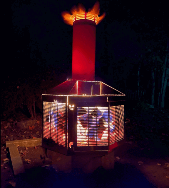 Stainless steel J.A. Roby Porthos outdoor fireplace with illuminated eight-sided design and chimney, perfect for backyard ambiance.