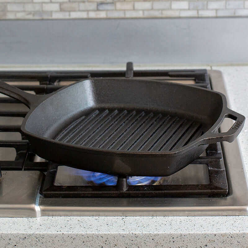 Lodge 10.5 inch cast iron square grill pan on stove, perfect for grilling with Cabin Depot quality. Seasoned surface, ready for delicious cooking.