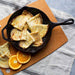 Cast iron skillet with crepes and orange slices on a cutting board.