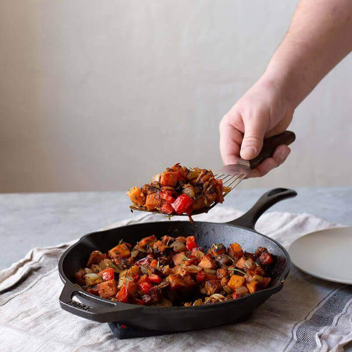 Chef using Lodge 10" Skillet with roasted vegetables, showcasing ergonomic handle and spatula-friendly design.