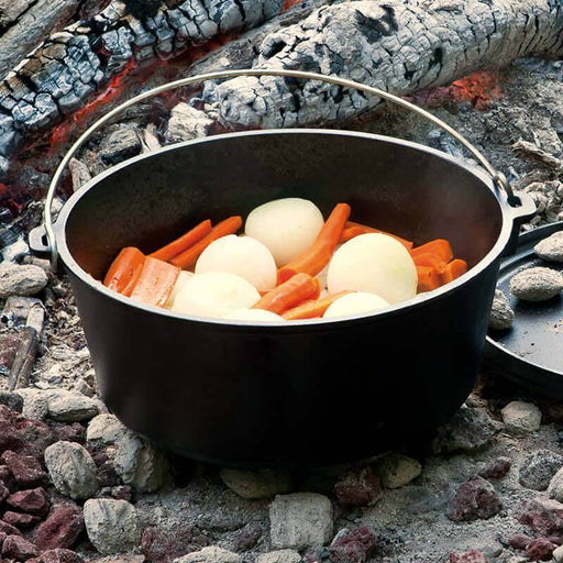 Lodge 12" 8 Quart Camp Dutch Oven cooking vegetables over campfire coals, showcasing its seasoned iron surface and sturdy design.