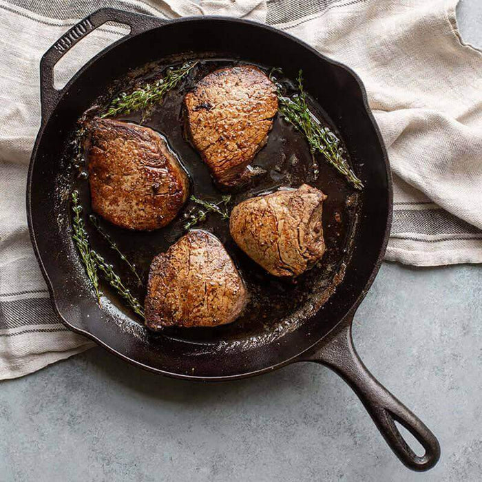 Lodge 12" Chef Collection Skillet with seared steaks and herbs, showcasing ergonomic design and superior heat retention.