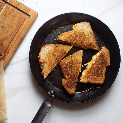 Lodge 12" seasoned steel skillet with grilled cheese sandwiches, showing even heat cooking and non-stick surface.