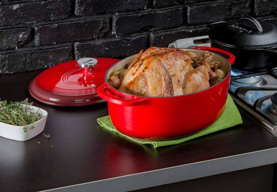 Red Lodge 7 Quart Oval Enameled Cast Iron Dutch Oven with roast chicken, shown on stovetop, showcasing versatility and style.