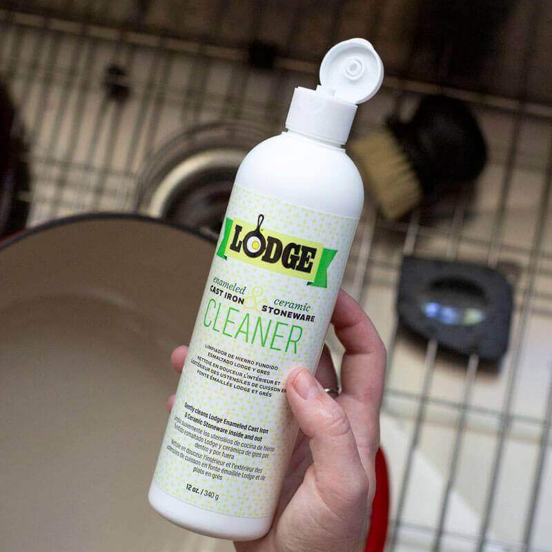 Lodge enamel cleaner from Cabin Depot for cast iron & stoneware care, biodegradable, bottle in hand, kitchen setting.