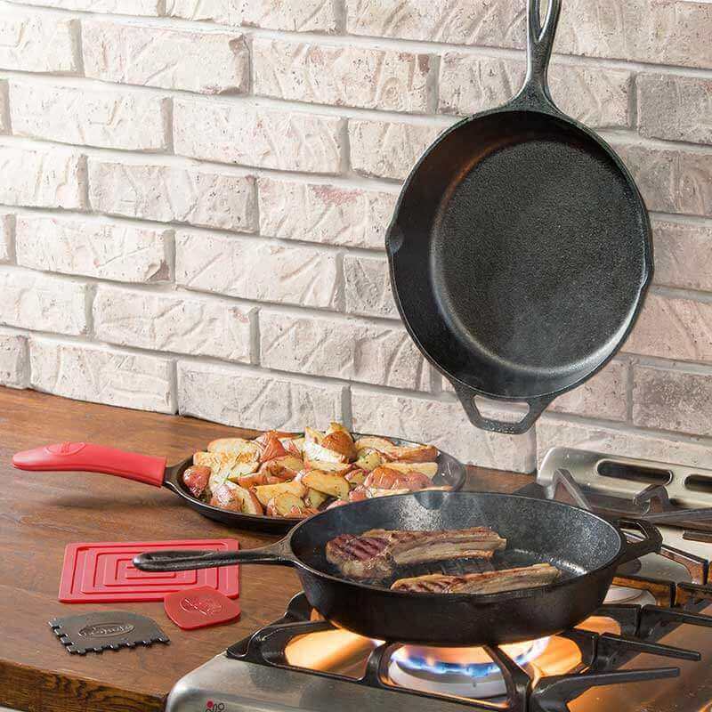Lodge Essential 6 Piece Pan Set cooking on stove, Cabin Depot cast iron skillets with steak and potatoes, seasoned for optimal meal preparation.