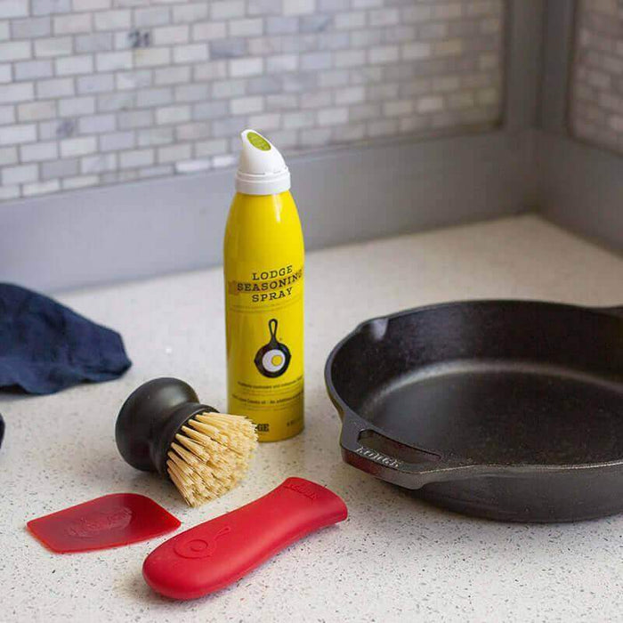 Lodge Seasoned Cast Iron Care Kit with scrub brush, seasoning spray, pan scraper, handle holder, and cast iron skillet on kitchen counter.