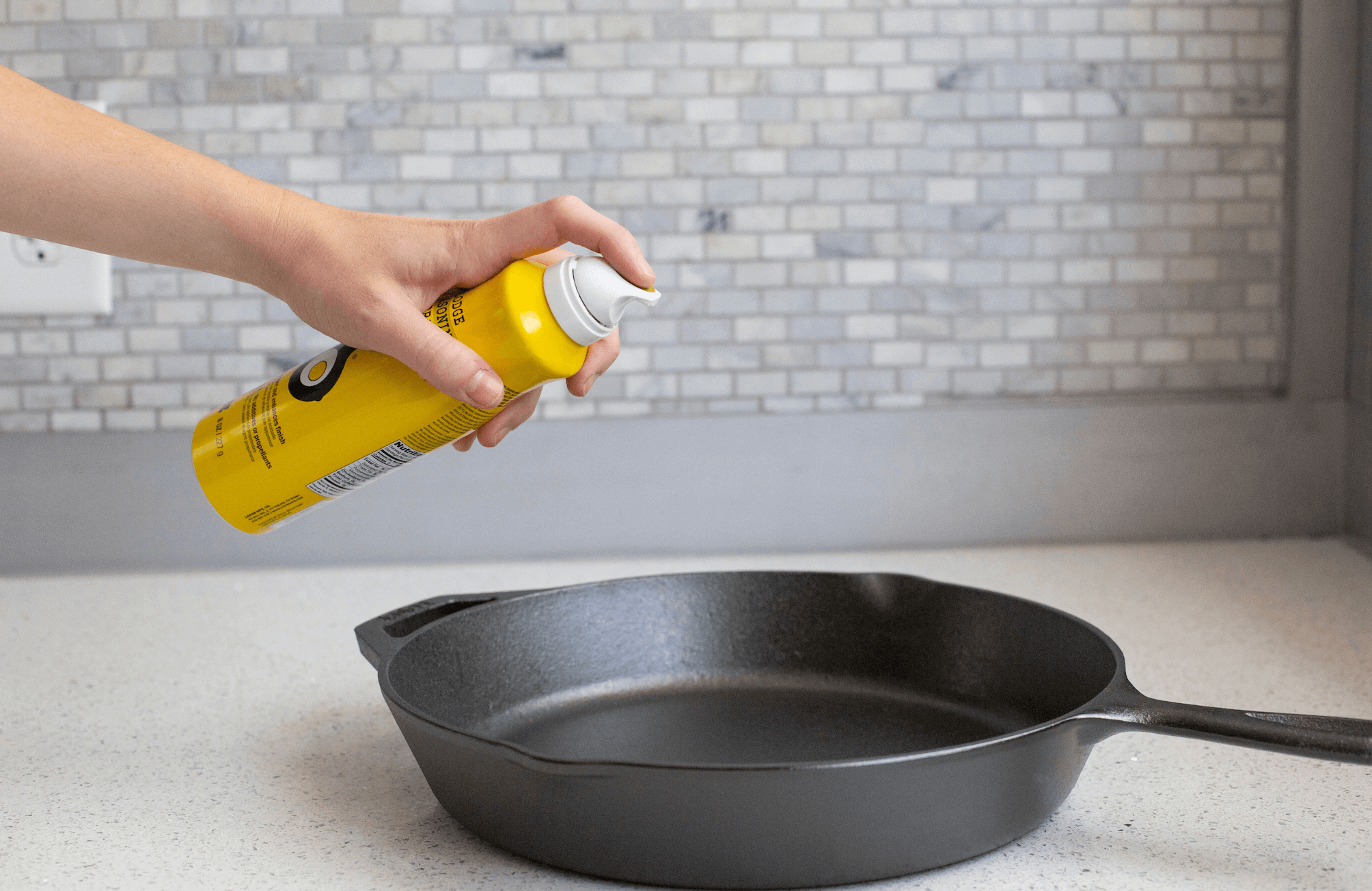 Applying Lodge Seasoning Spray to cast iron skillet, enhances finish, 100% canola oil, sold at Cabin Depot.