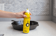 Hand holding Lodge Seasoning Spray can next to cast iron skillet on kitchen counter.