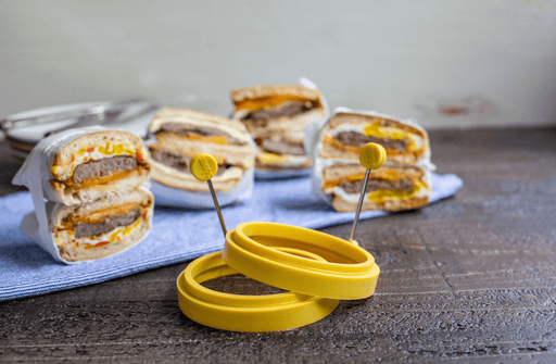 Yellow Lodge silicone egg rings on a table with breakfast sandwiches in the background, perfect for making round fried eggs.