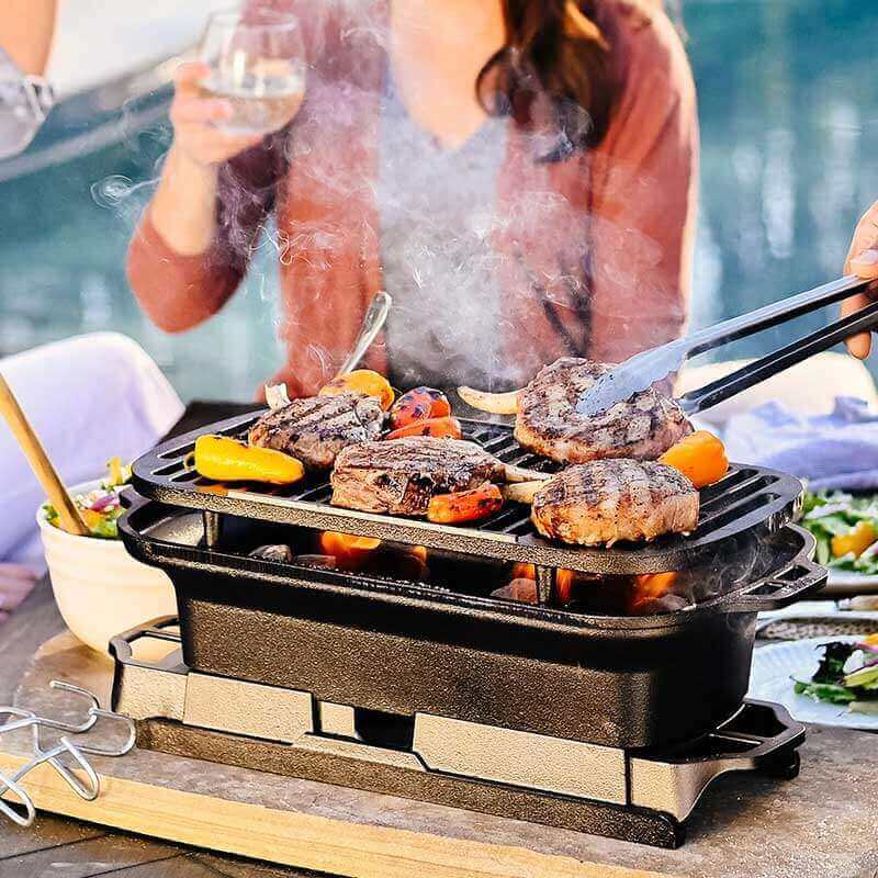 Lodge Sportsman's Pro Cast Iron Grill in use, featuring sizzling burgers and vegetables, perfect for backyard BBQs. Available at Cabin Depot.