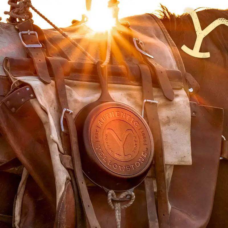 Lodge 10.25" Yellowstone Cast Iron Skillet with Dutton Ranch Y design on saddle at sunrise, available at Cabin Depot.