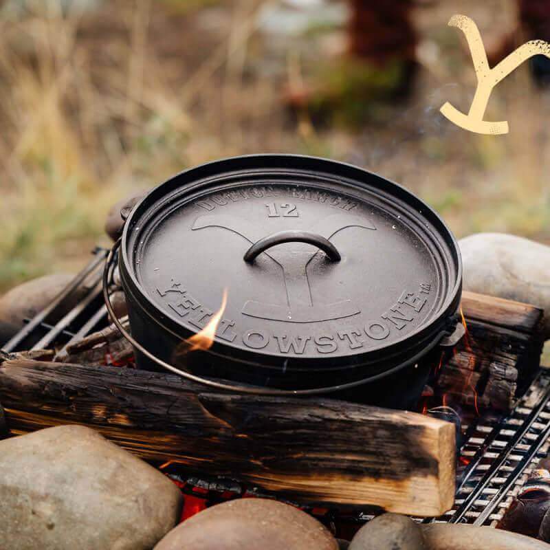 Lodge 12" Yellowstone cast iron dutch oven on campfire, featuring Power Y lid, perfect for outdoor cooking. Available at Cabin Depot.