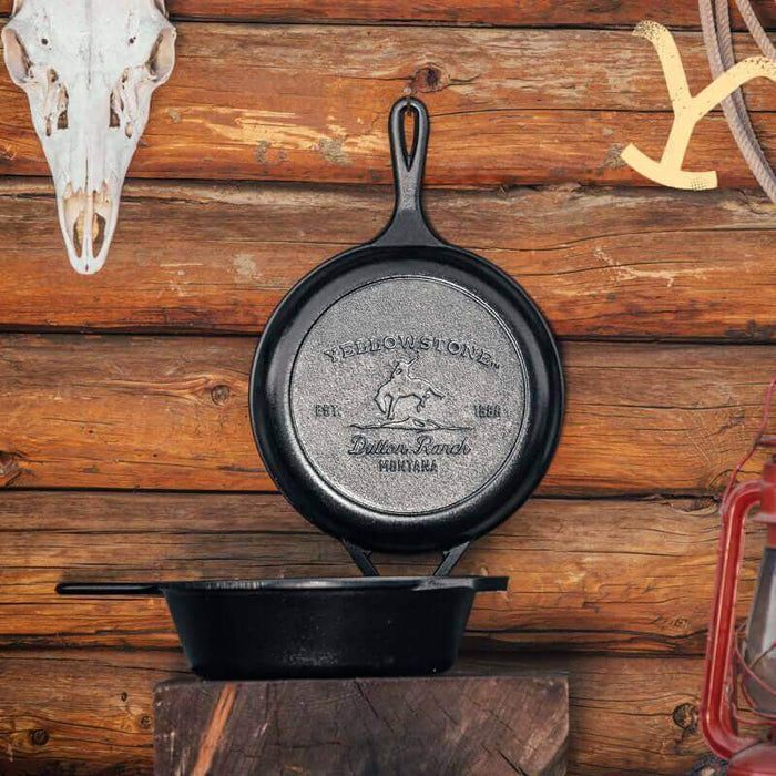 Lodge Yellowstone cast iron combo cooker with bucking bronco design on lid, set against a rustic wooden background.