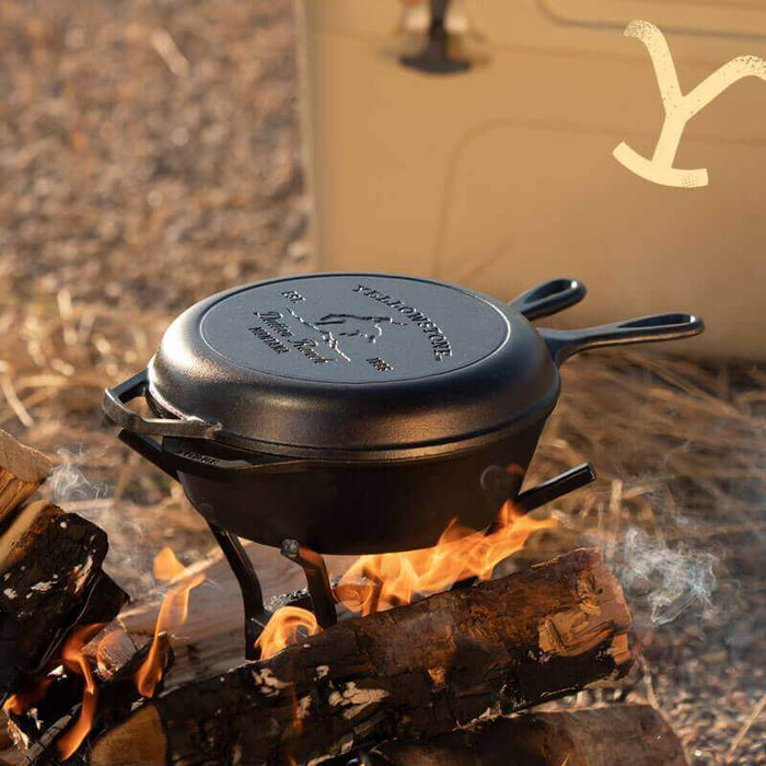 Lodge Yellowstone cast iron combo cooker with bucking bronco design on lid, sitting on campfire, perfect for outdoor cooking.