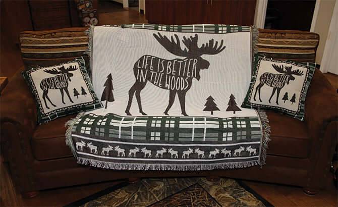 Moose-themed tapestry throw and pillows on a sofa; decor for cabins - "Life is Better in the Woods."