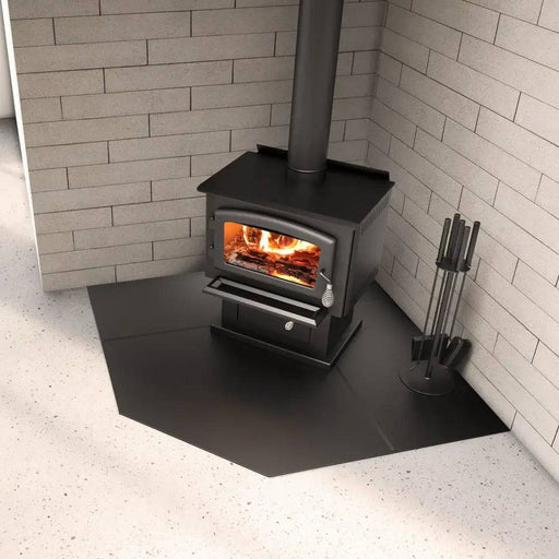 Black wood stove on SBI 54" corner hearth pad with brick wall background, designed to protect floors from hot embers.