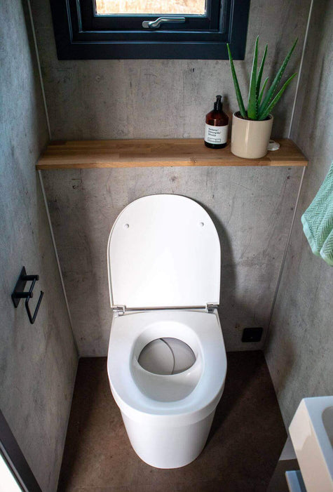 Compact Separett Tiny 1271 Toilet in modern washroom setting with plant and soap on shelf. Perfect for small spaces like RVs and cabins.