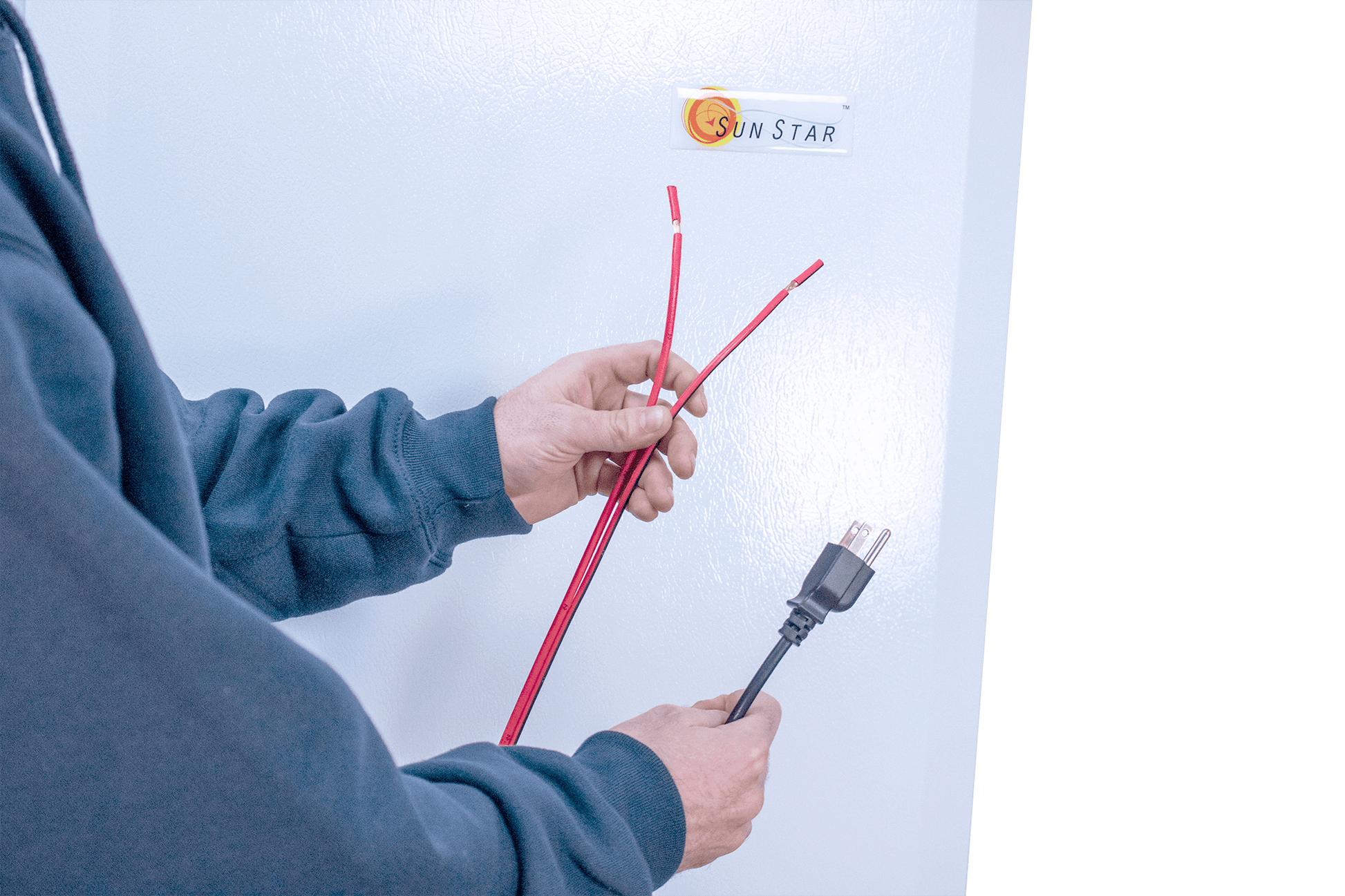 Person holding power cables next to SunStar 10CU Solar DC/AC Refrigerator at Cabin Depot
