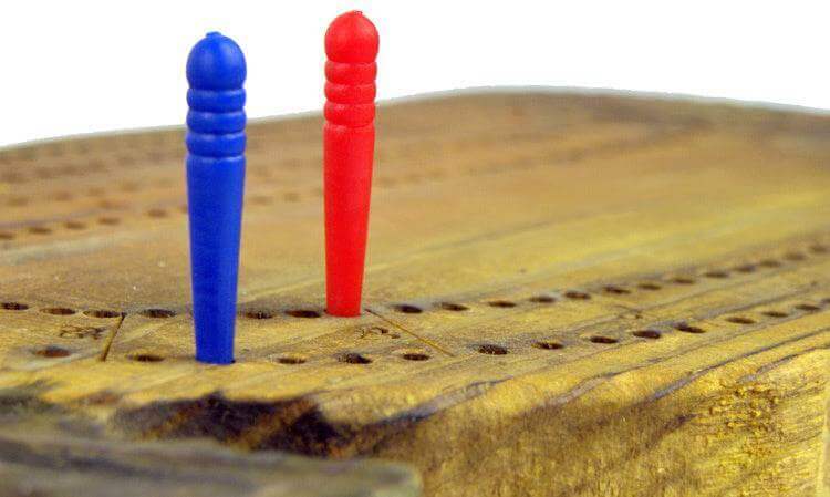 Close-up of hand-carved wooden cribbage board with blue and red pegs, sold by Cabin Depot.