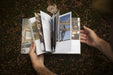 Person flipping through pages of the Cabin Porn Inside book in a natural outdoor setting.