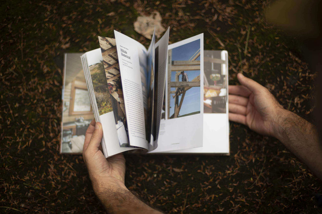 Person flipping through pages of the Cabin Porn Inside book in a natural outdoor setting.