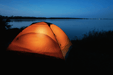 Illuminated tent by a lakeside at night, showcasing outdoor camping setup.