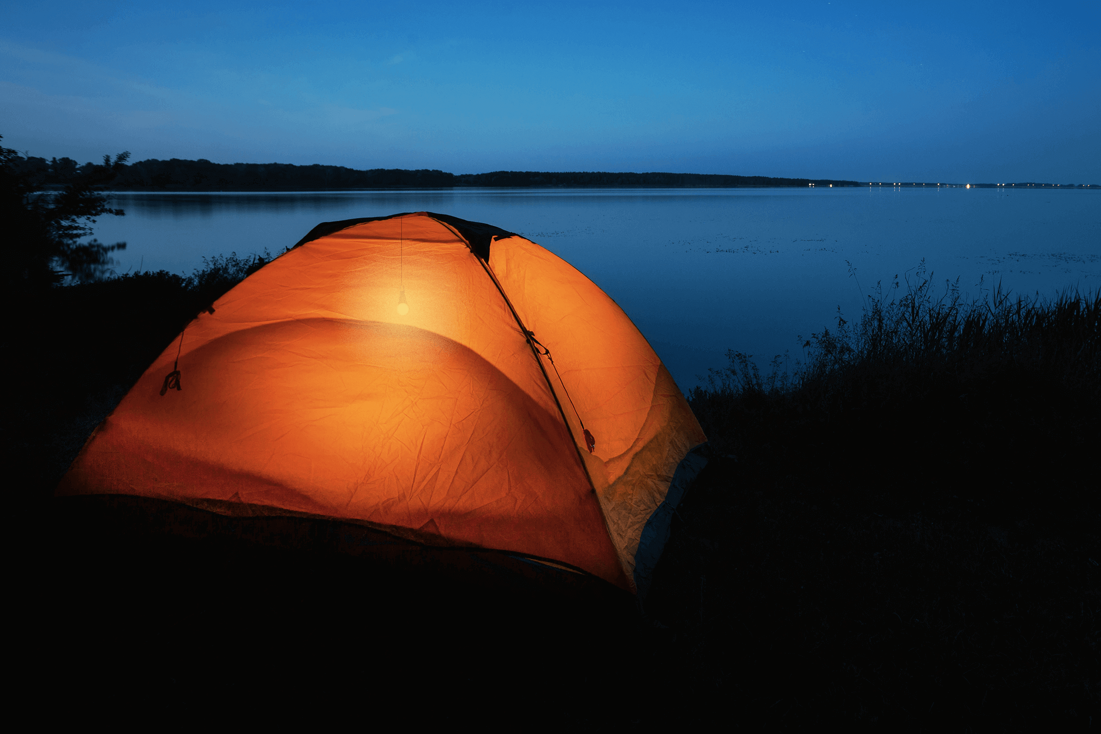 Orange tent illuminated at night by Kedron 12V camp light near a lake, highlighting outdoor camping environment.