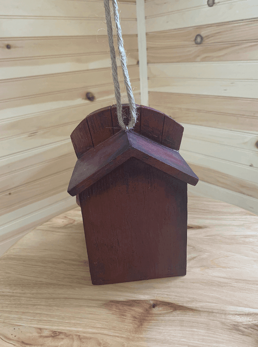 Rustic Adirondack chair-shaped birdhouse with rope hanger against wooden background. Perfect for attracting birds to your garden.