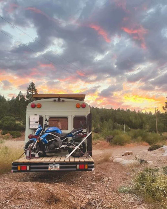 Motorcycle loaded onto van at sunset with a scenic outdoor backdrop.