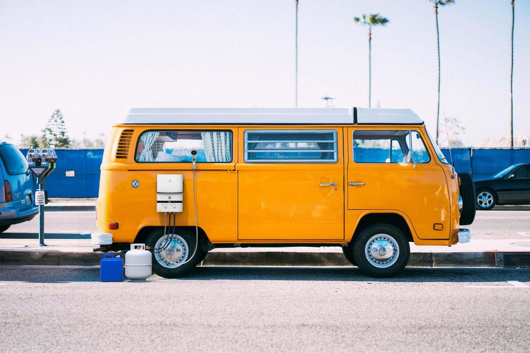 Bright yellow vintage van parked on a sunny street with palm trees in the background.