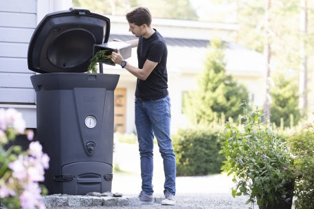 Man using Biolan Biowaste 220 Eco Composter for kitchen waste composting outdoors, available at Cabin Depot, with insulated design.