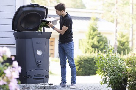 Man using Biolan 220 ECO Composter in garden for efficient kitchen waste composting.